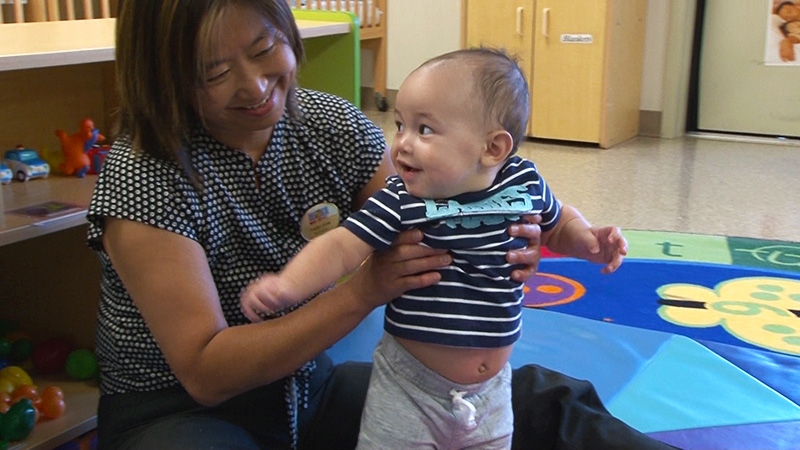 A staff member holds a toddler to help him stand